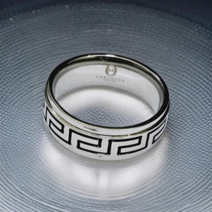 Stainless steel Greek key pattern ring by T.M.J, showcasing intricate design and polished finish on a sleek stainless steel band.