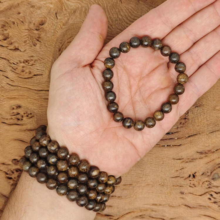 Natural Bronzite Stone Beads Bracelet in hand with wood background.