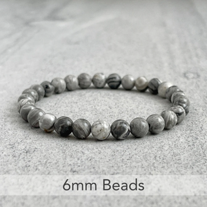 Natural gray jasper beads bracelet with 6mm stones arranged in a circle on a marble surface.