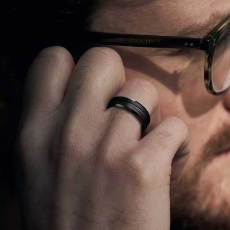 Black tungsten carbide ring with polished center groove and matte finish on man's hand.