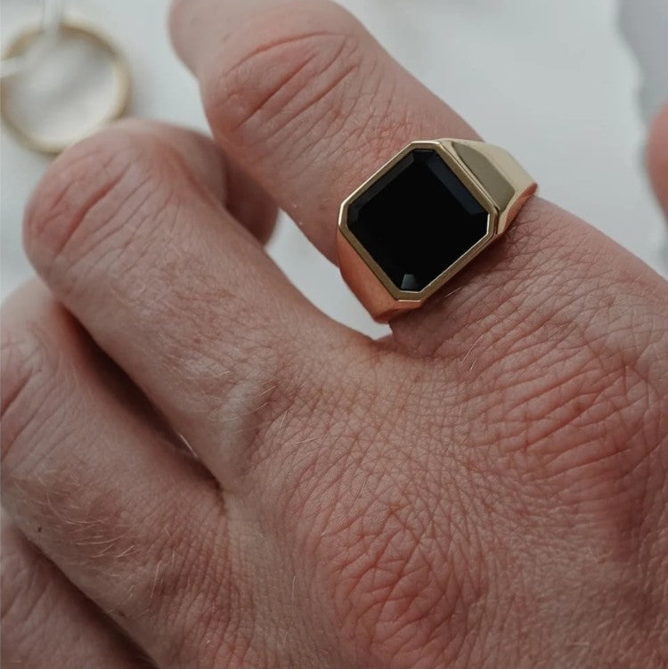 Stainless steel ring with black stone on hand, showcasing a matte finish and bold design.