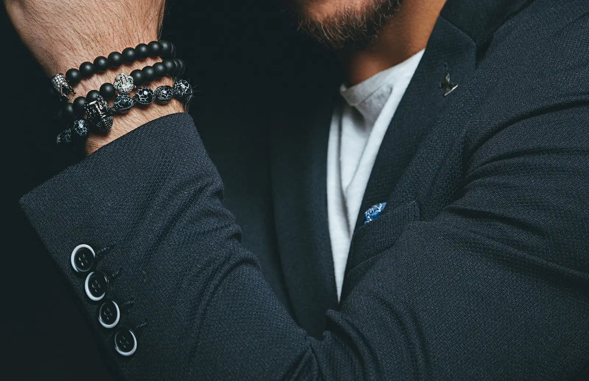 Man in a dark tailored suit wearing black beaded bracelets on his wrist