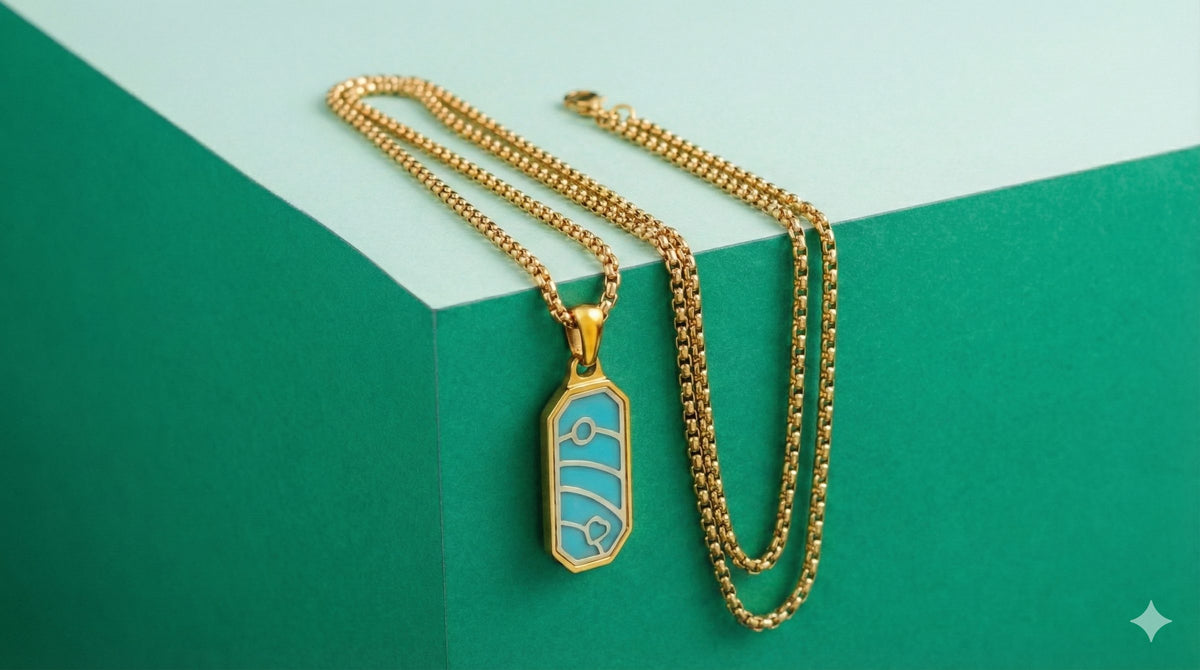 Gold box chain necklace with a turquoise pendant on a green and mint background