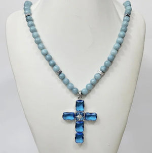 Large silver cross pendant with Austrian crystals on aquamarine beaded necklace by T.M.J, elegant and vibrant jewelry accessory.