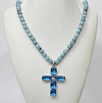 Large silver cross pendant with Austrian crystals on aquamarine beaded necklace by T.M.J, elegant and vibrant jewelry accessory.