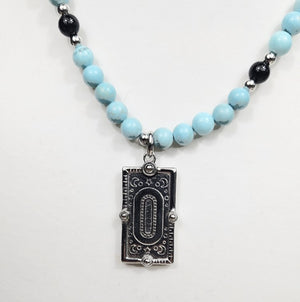 Silver enamel snake dog tag pendant on a turquoise beaded necklace, stylish T.M.J jewelry accessory.