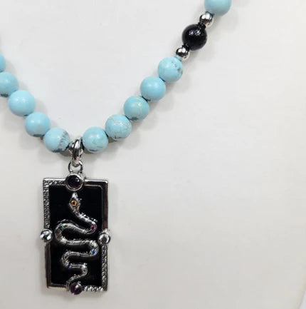 Silver enamel snake dog tag pendant on a turquoise beaded necklace, stylish jewelry by T.M.J with detailed design.