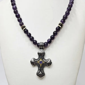 Stainless steel cross pendant with amethyst crystal on purple beaded necklace, by T.M.J, close-up view of the jewelry.