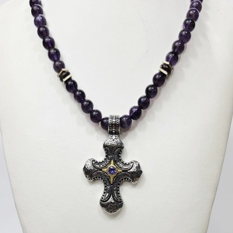Stainless steel cross pendant with amethyst crystal on purple beaded necklace, by T.M.J, close-up view of the jewelry.
